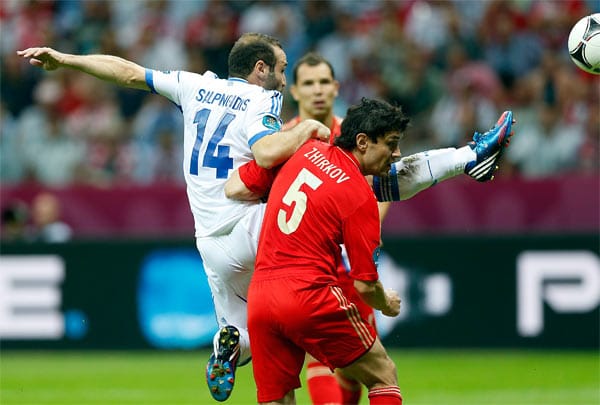 Dimitris Salpingidis klärt den Ball mit vollem Körpereinsatz. Der Russe Yuri Zhirkow zieht gerade noch den Kopf weg. Dimitris Salpingidis klärt den Ball mit vollem Körpereinsatz. Der Russe Yuri Zhirkow zieht gerade noch den Kopf weg.
