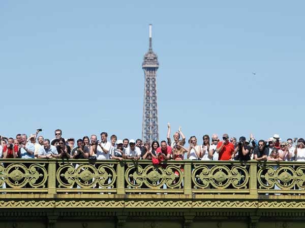 Kaiserwetter in Paris. Diese Fans schauen sich die letzte Etappe von einer Brücke aus an. Im Hintergrund ist die Spitze des Eiffelturms zu sehen.