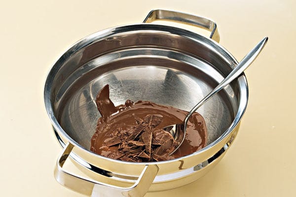 Die Schüssel mit der geschmolzenen Kuvertüre aus dem Wasserbad nehmen und die restliche kalte Schokolade nach und nach unterrühren.