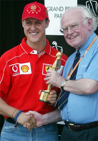 Formel-1-Weltmeister Michael Schumacher (Ferrari/li.) erhält im September 2002 auf der Rennstrecke in Indianapolis (US-Bundesstaat Indiana) von Rennarzt Sid Watkins (re.) den "Bernie" als bester Fahrer des Jahres. Die dem Oscar nachempfundenen Trophäen in Form des Formel-1-Chefs Bernie Ecclestone wurden neben Schumacher an Kimi Räikkönen (Einsteiger des Jahres), Frank Williams (Lebenswerk), Paul Stoddart (besondere Leistungen) und Ross Brawn (Technik) verliehen.