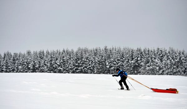 Skitourer zieht Pulka hinter sich her.