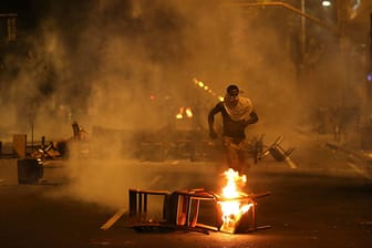 Feuerteufel: Ein Randalierer rennt zwischen brennenden Stühlen durch eine Straße in Rio de Janeiro. Nach einer friedlichen Demonstration von Lehrern war es in der brasilianischen Metropole zu Straßenschlachten zwischen der Polizei und Mitgliedern des "Black Block" gekommen.