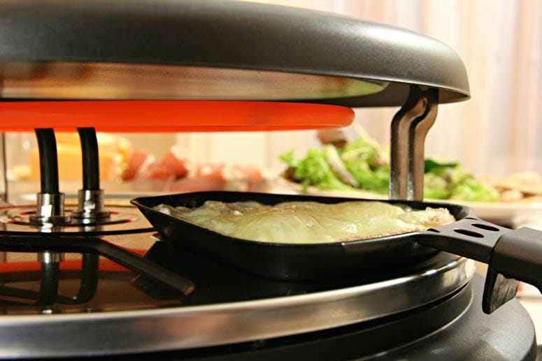 Der Käse wird in einem elektrisch betriebenen Raclettegerät geschmolzen.