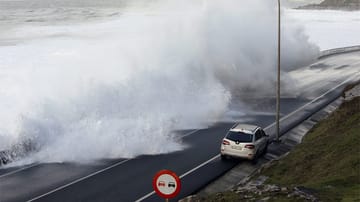 Dieses Verkehrsschild sollte besser befolgt werden: Eine hohe Welle kracht auf eine Küstenstraße in der Nähe des Dorfes Baiona in Galizien.