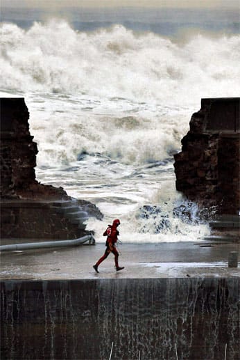 Ein Mitarbeiter des Roten Kreuzes läuft neben einer zerstörten Kaimauer im Hafen von Bermeo. Das Wasser strömt vom Meer unter seinen Füßen in Richtung der Stadt.