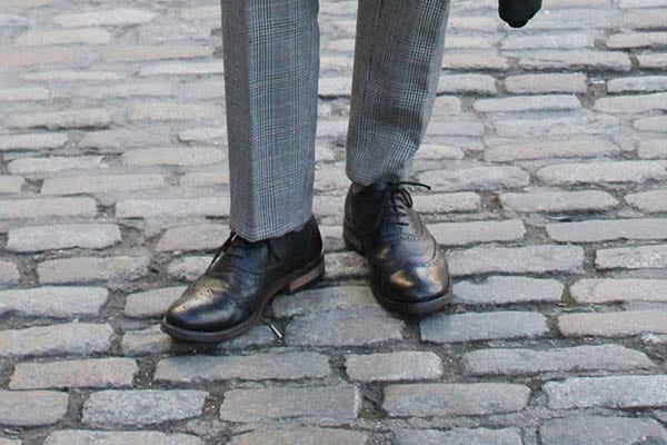 Zu der grauen Anzughose kombiniert George schwarze Halbschuhe aus Glattleder – wieder sehen wir hier das typisch britische Lochmuster.