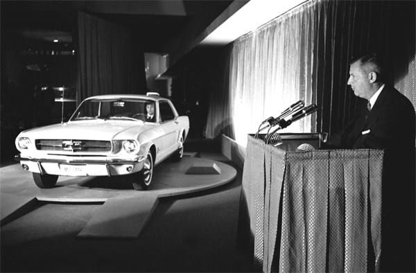 Lee Iacocca bei der Weltpremiere des Ford Mustang. Der Sportwagen basierte auf dem Ford Falcon. Das Basismodell fährt nur mit einem Sechszylinder mit 2,8 Litern Hubraum und 102 PS. Doch schon zum Start gab es auch einen Mustang mit einem V8-Motor, der aus 4,7 Litern Hubraum 275 PS schöpft.