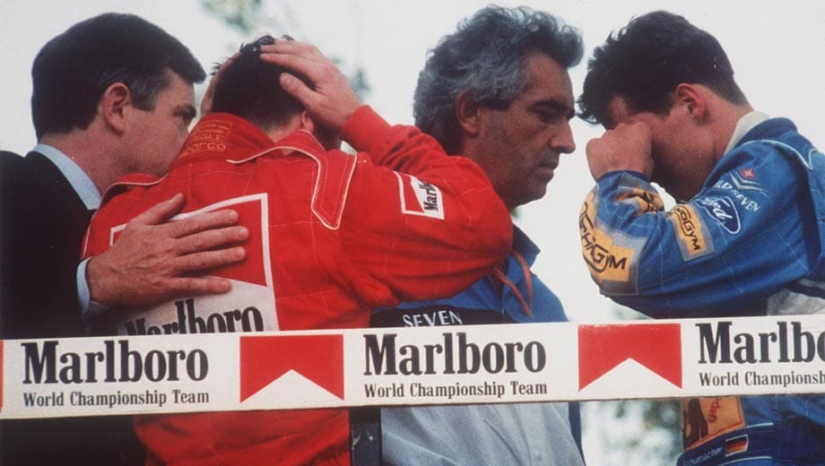 Das Rennen in Imola wird nicht abgebrochen. Michael Schumacher (re.) gewinnt. Als die Piloten vom kritischen Zustand Sennas erfahren, sind sie sichtlich geschockt. (2.v.li. Nicola Larini, Mitte: Flavio Briatore, damals Teamchef von Schumacher bei Benetton).