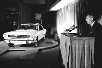 Lee Iacocca bei der Weltpremiere des Ford Mustang. Der Sportwagen basierte auf dem Ford Falcon. Das Basismodell fährt nur mit einem Sechszylinder mit 2,8 Litern Hubraum und 102 PS. Doch schon zum Start gab es auch einen Mustang mit einem V8-Motor, der aus 4,7 Litern Hubraum 275 PS schöpft.