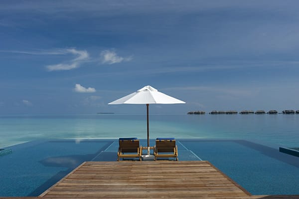 Der Infinity-Pool des Conrad Maledives scheint das Meer zu küssen. Unter dem leuchtend blauen Himmel der Malediven macht das Relaxen im Hotelpool besonders viel Spaß.