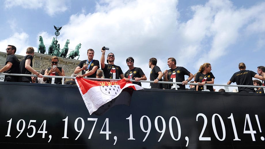 Im offenen Bus fahren die Nationalspieler durch die Hauptstadt. Köln-Ikone Lukas Podolski 5.v.li.) hat die Fahne seiner Stadt dabei.