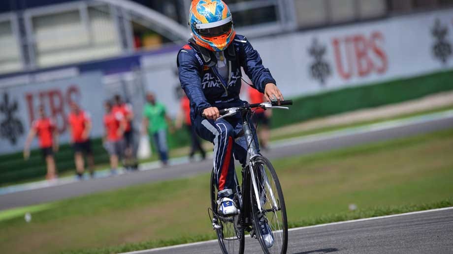 Streckeninspektion einmal ganz anders: Der GP2-Pilot Artjom Markelow fährt mit Rennanzug und Helm Fahrrad auf dem Hockenheimring.