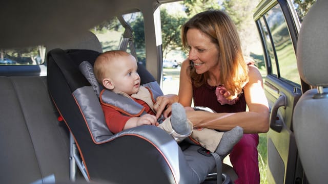 Frau schnall Kind im Kindersitz vom Auto an.