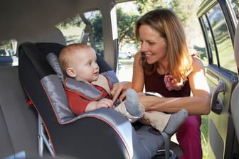 Frau schnall Kind im Kindersitz vom Auto an.