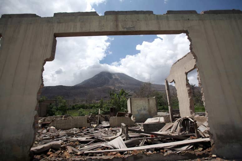 Blick auf ein bröckelndes Gebäude im Dorf Simacem in Nord-Sumatra, Indonesien. Im Hintergrund zu sehen ist der 2600 Meter hohe Vulkan Sinabung, einer der 130 aktiven Vulkane Indonesiens. Nach 400 Jahren Ruhe brach dieser 2010 aus. Mehr als 22.000 Menschen mussten evakuiert werden.