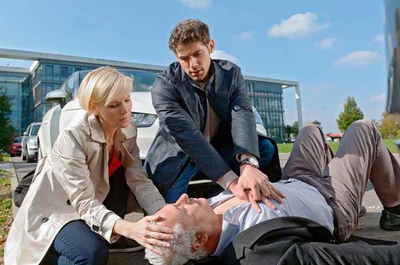 Vor der Klinik finden die beiden Dr. Harald Lossen (Robert Giggenbach, liegend). Er hatte einen Herzinfarkt. Die Ärzte leisten sofort Erste Hilfe.