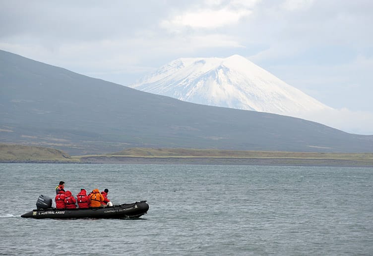 Touristen fahren bei Schumschu in Schlauchbooten zurück zum Kreuzfahrtschiff. Im Hintergrund ist der Vulkan Alaid zu sehen.