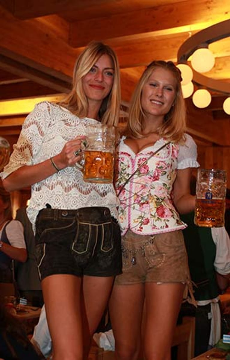 Die Schauspielerin Maximilane Bauer und das Model Julie Göllner in kurzen Lederhosen und mit Bierkrug.