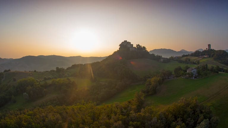 Die Burg Rossena thront über der Landschaft, umgeben von malerischen Hügeln, Gutshöfen und Weinreben.
