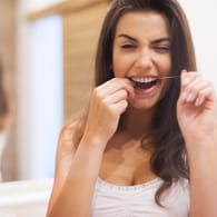 Frau benutzt Zahnseide: Zahnseide ist wichtig, da Zahnzwischenräume eine erhöhte Kariesgefahr bergen.