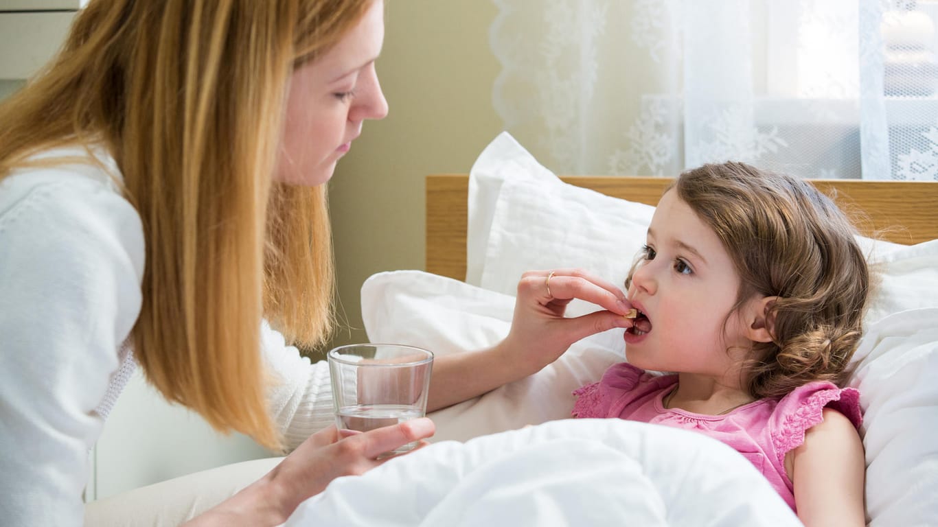 Mutter legt im Bett liegenden Kind Tablette in den Mund