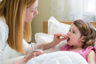 Mutter legt im Bett liegenden Kind Tablette in den Mund