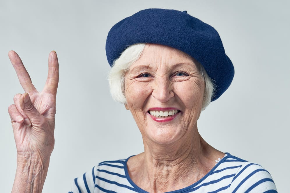 Eine ältere Frau zeigt das Peace-Symbol: Das wär doch was, als Frau mit 60 in Rente gehen. So einfach geht das nicht und kommt auch kaum noch zur Anwendung.
