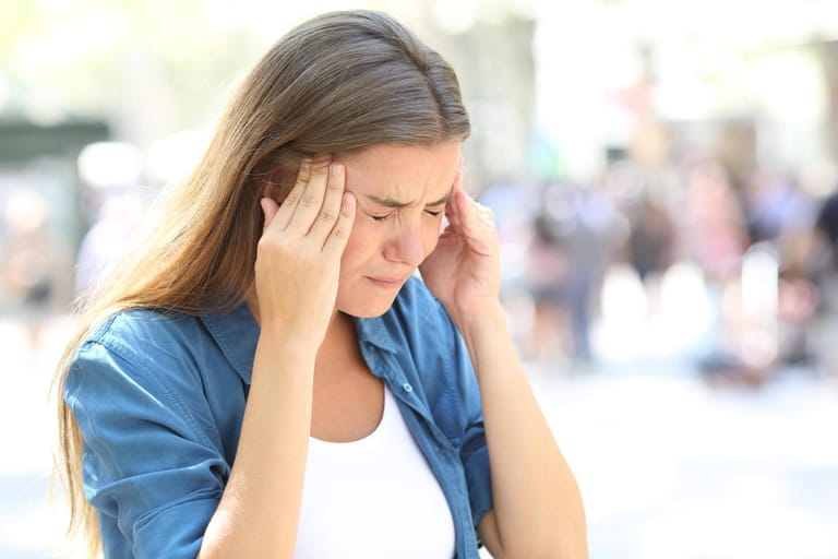 Frau hält sich die Schläfen: Bei einem Schlaganfall können Blutungen im Gehirn entstehen, die starke Kopfschmerzen auslösen. Übelkeit und Erbrechen sind weitere mögliche Begleiterscheinungen.