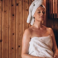 Eine Frau in der Sauna: Beim Saunagang darf die Haut nicht mit dem Holz in Kontakt kommen. An Stellen, auf denen die Haut aufliegt, muss ein Handtuch gelegt werden.