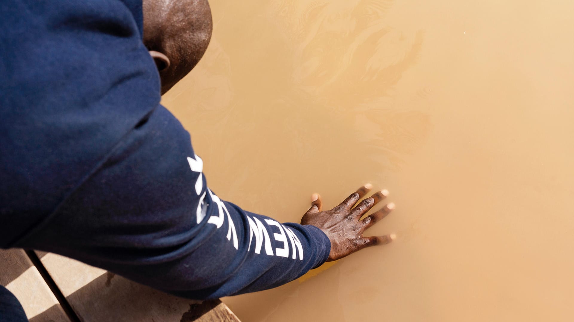 Ein Gläubiger beugt sich zum Fluss hinunter und hält seine Hand in das trübe Wasser.