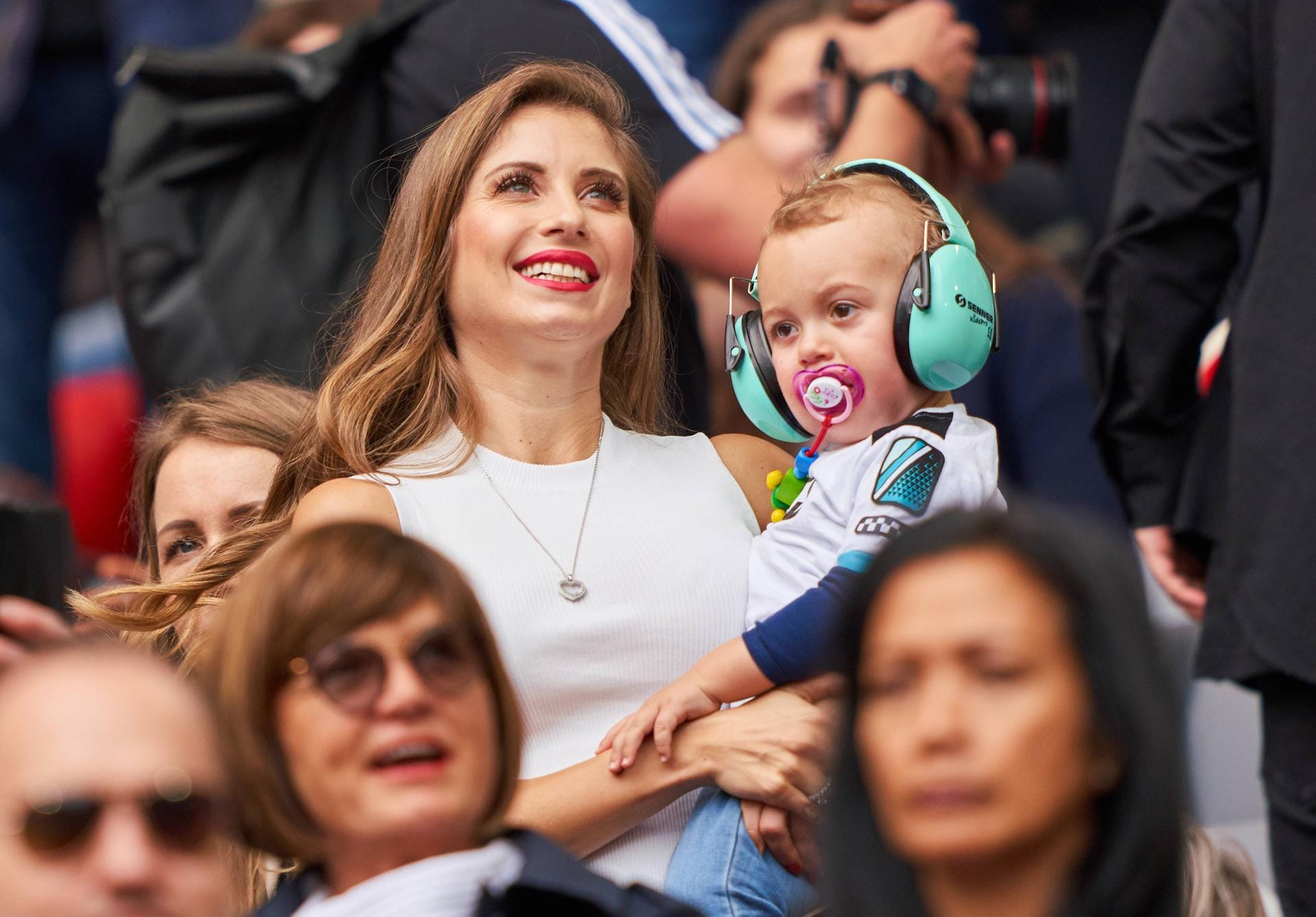 2019: Bei den Besuchen der Fußballspiele vom Papa, trägt Sohn Ludwig türkisfarbene Schutzhörer gegen den Stadionlärm, während er bei Mama auf dem Arm ist.