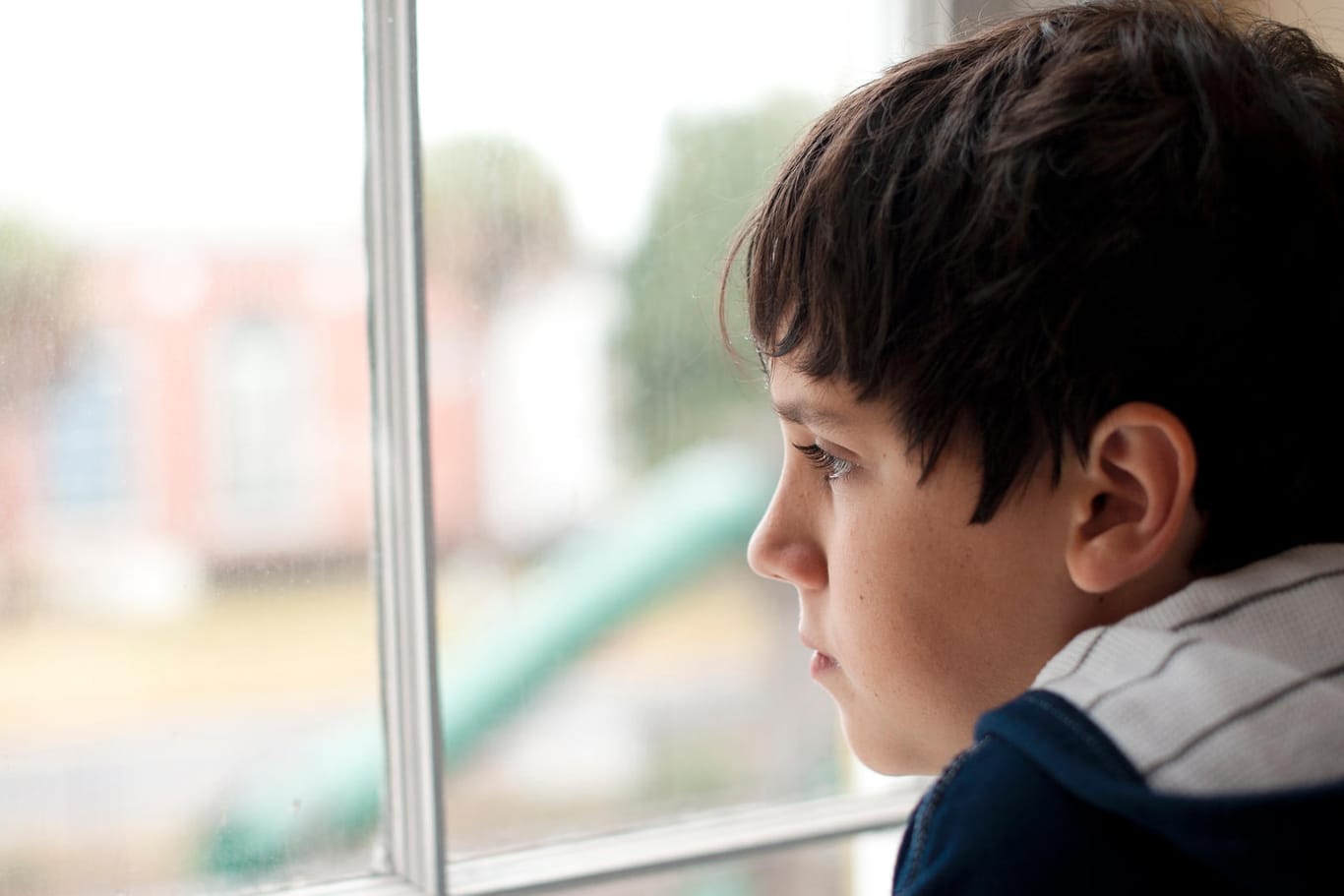 Ein einsam wirkender Junge schaut aus dem Fenster: Menschen mit Autismus wirken auf Außenstehende oft zurückgezogen und abweisend.