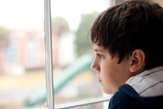 Ein einsam wirkender Junge schaut aus dem Fenster: Menschen mit Autismus wirken auf Außenstehende oft zurückgezogen und abweisend.