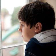 Ein einsam wirkender Junge schaut aus dem Fenster: Menschen mit Autismus wirken auf Außenstehende oft zurückgezogen und abweisend.