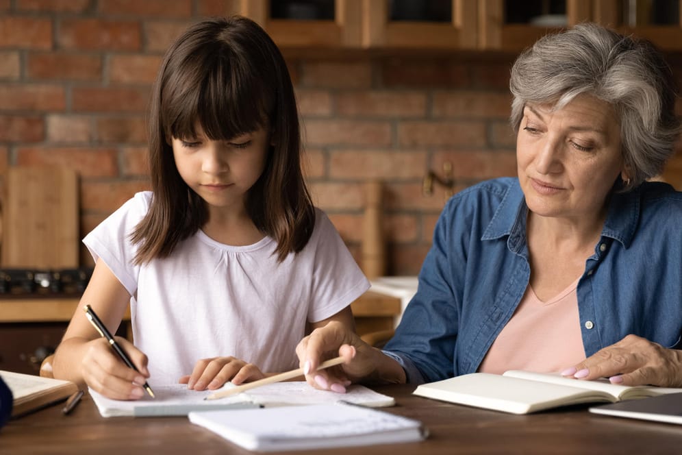Oma hilft ihrer Enkeltochter bei den Hausaufgaben (Symbolbild): Inwiefern zählen Betreuungszeiten des Enkelkindes für die eigene Rente?