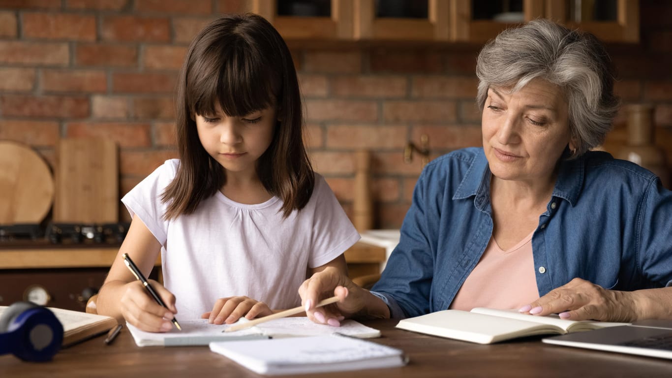 Oma hilft ihrer Enkeltochter bei den Hausaufgaben (Symbolbild): Inwiefern zählen Betreuungszeiten des Enkelkindes für die eigene Rente?