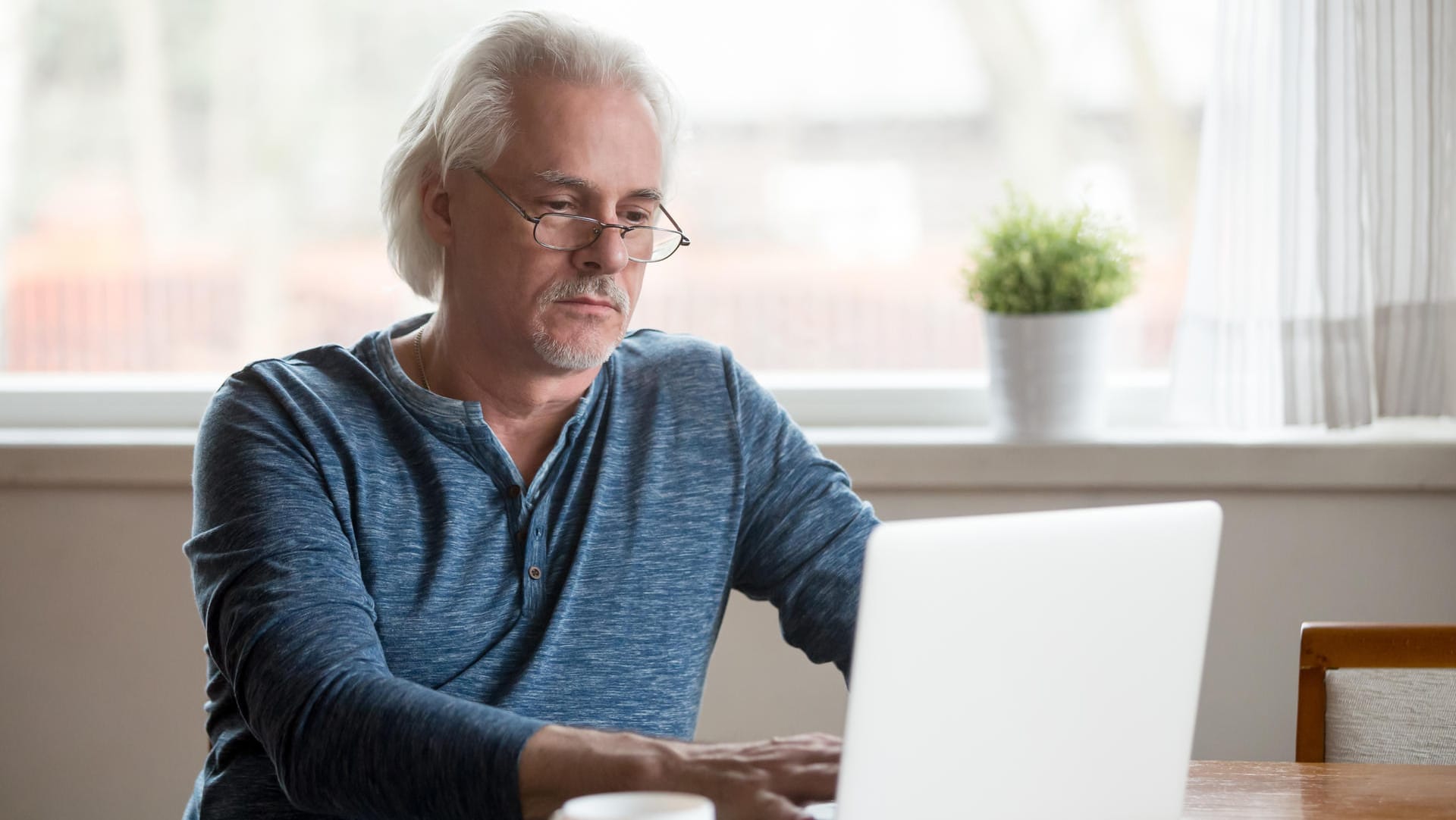 Ein älterer Mann am Laptop (Symbolbild): Es ist möglich, neben Beamtenpension auch gesetzliche Rente zu erhalten.