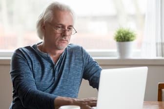 Ein älterer Mann am Laptop (Symbolbild): Es ist möglich, neben Beamtenpension auch gesetzliche Rente zu erhalten.