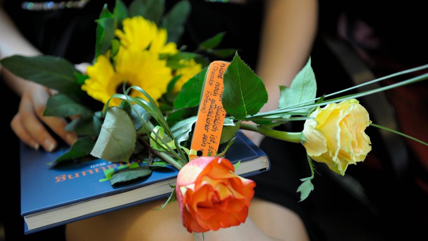 Jugendweihe: Teilnehmerin hat Buchgeschenk und Blumen auf dem Schoß.