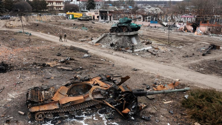 Ukraine, Trostjanez: Anwohner gehen an einem beschädigten russischen Panzer in der Stadt Trostyanets, östlich der ukrainischen Hauptstadt Kiew, vorbei; im Hintergrund steht ein Denkmal zur Erinnerung an den Zweiten Weltkrieg.
