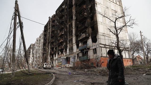 Eine Frau geht an einem beschädigten Gebäude in Mariupol vorbei.