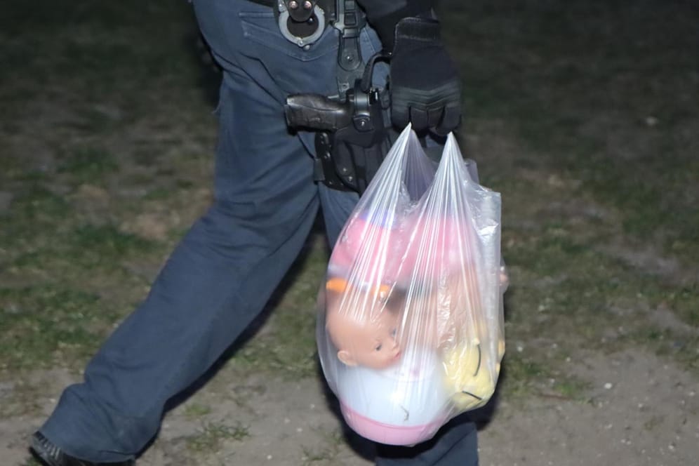 Ein Polizist hat Kuscheltiere und Puppen in einer Tüte gesammelt: Das Spielzeug lag verteilt auf dem Rasen vor dem Wohnhaus.