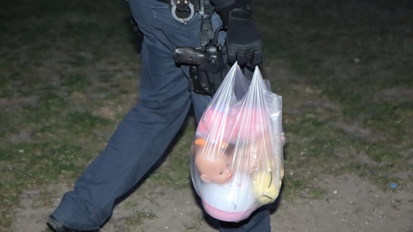 Ein Polizist hat Kuscheltiere und Puppen in einer Tüte gesammelt: Das Spielzeug lag verteilt auf dem Rasen vor dem Wohnhaus.