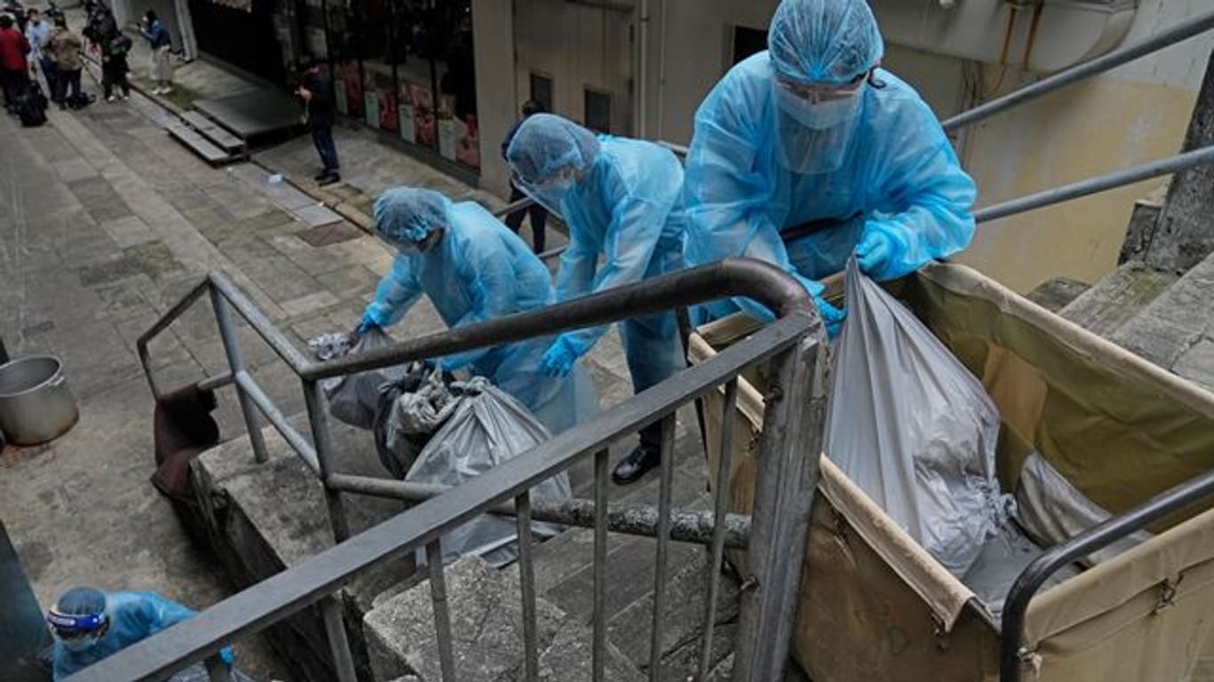 Hotelangestellte in Hongkong tragen Schutzkleidung und entsorgen Müll aus einem Hotel, das zur Isolation genutzt wird.