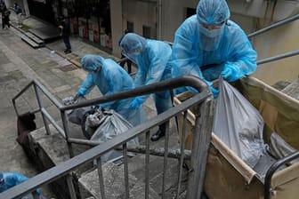 Hotelangestellte in Hongkong tragen Schutzkleidung und entsorgen Müll aus einem Hotel, das zur Isolation genutzt wird.