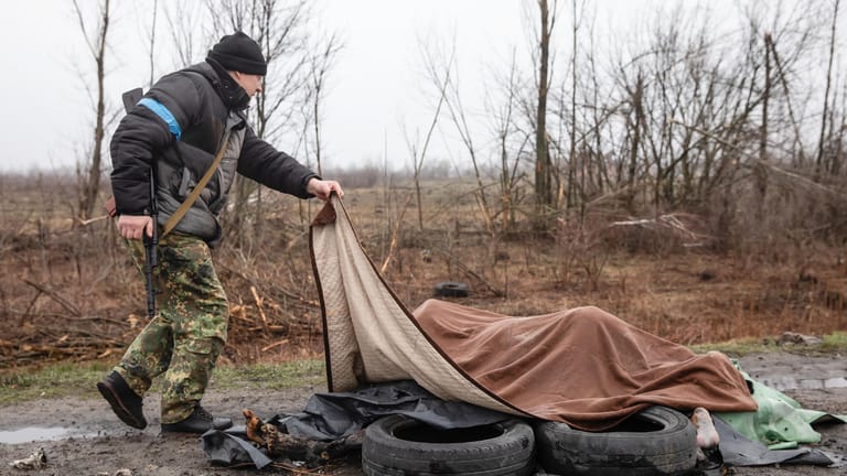 Ein Mitglied der zivilen Schutztruppe betrachtet unter einer Decke am Rande der Autobahn, 20 Kilometer von Kiew entfernt, vier tote Zivilisten.