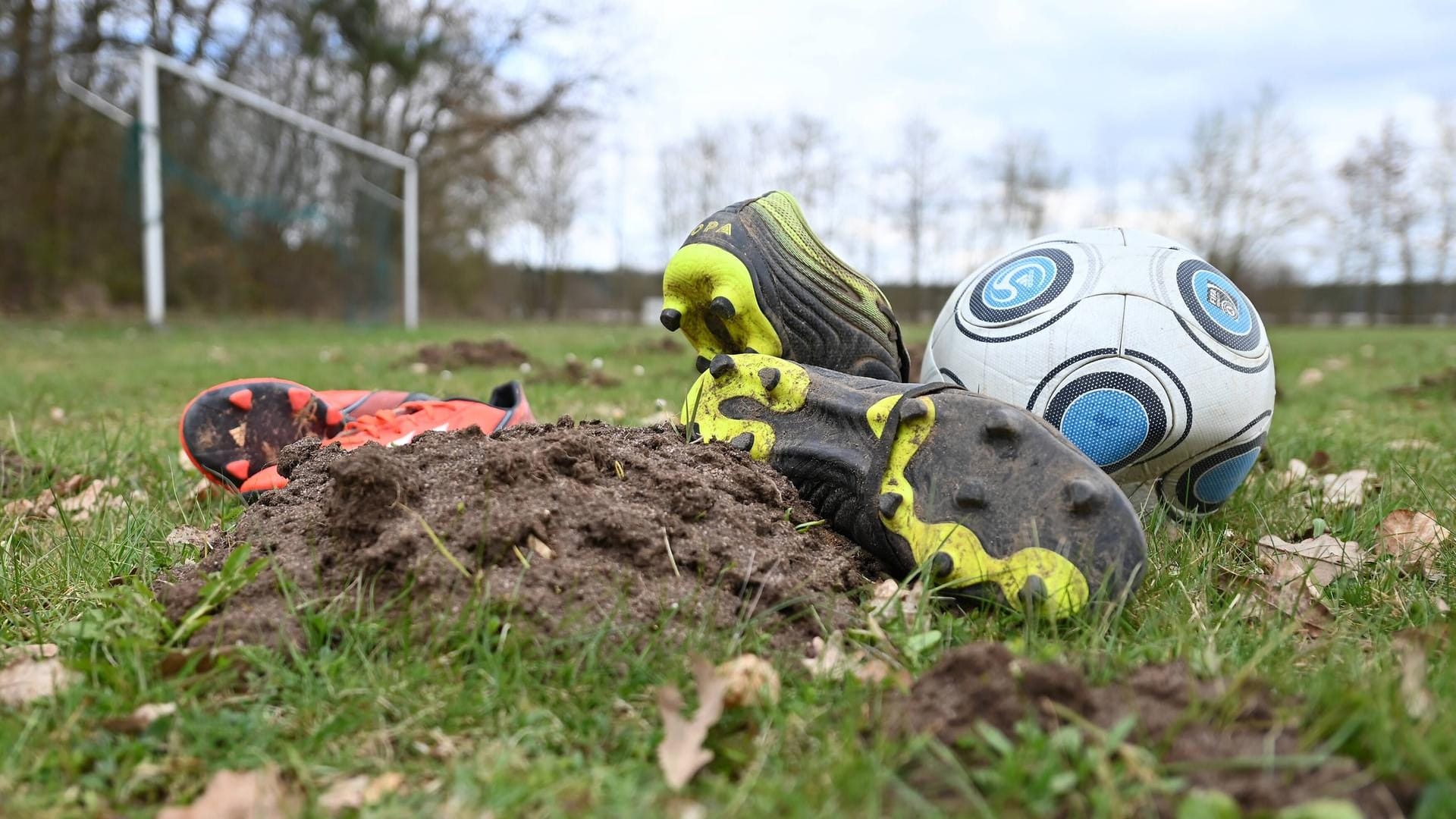 Ein platter Fußball und Stollenschuhe liegen auf einem durchpflügten Fußballfeld (Symbolbild): In der Bremer Vahr ist ein Pokalspiel der A-Jugend nach einer Prügelei abgebrochen worden.