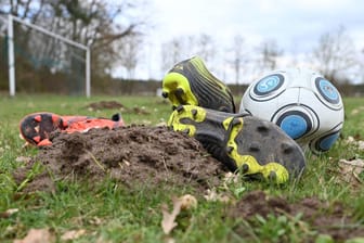Ein platter Fußball und Stollenschuhe liegen auf einem durchpflügten Fußballfeld (Symbolbild): In der Bremer Vahr ist ein Pokalspiel der A-Jugend nach einer Prügelei abgebrochen worden.