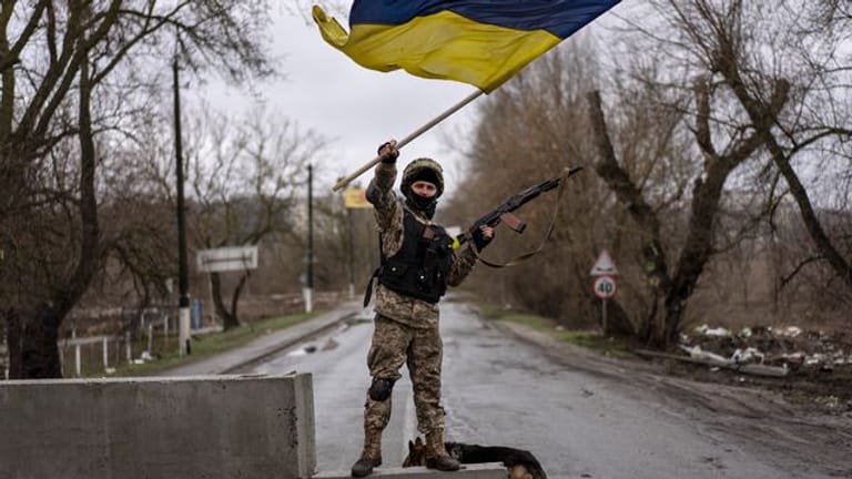 Ein ukrainischer Soldat steht an einer Straßenblockade und hält die ukrainische Flagge hoch.