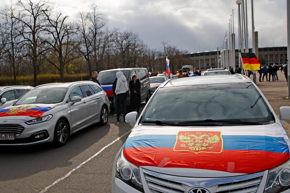 Flaggen mit den russischen Nationalfarben, dem russischen Staatswappen sowie eine deutsche Fahne sind an mehren Autos am Ende eines Autokorsos auf dem Olympiaplatz vor dem Olympiastadion befestigt.